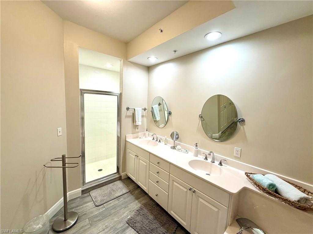 Full bath with a shower stall, light wood-type flooring, and double vanity