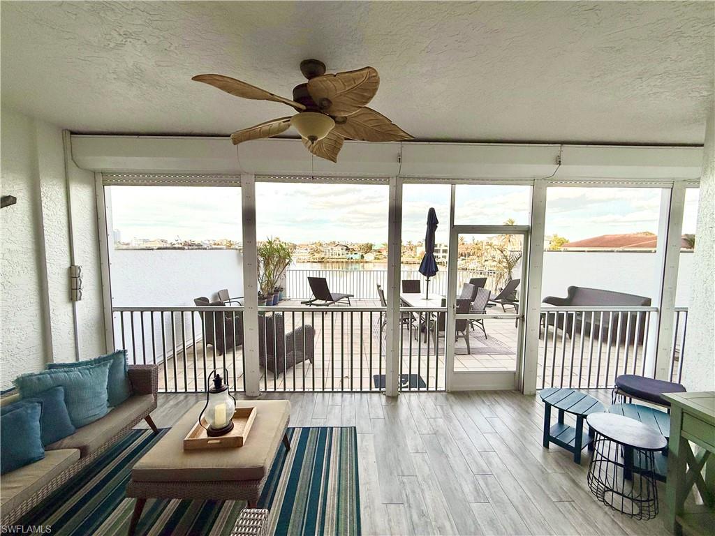 Sunroom / solarium with ceiling fan, a water view, a textured ceiling, wood finished floors, and an outdoor hangout area