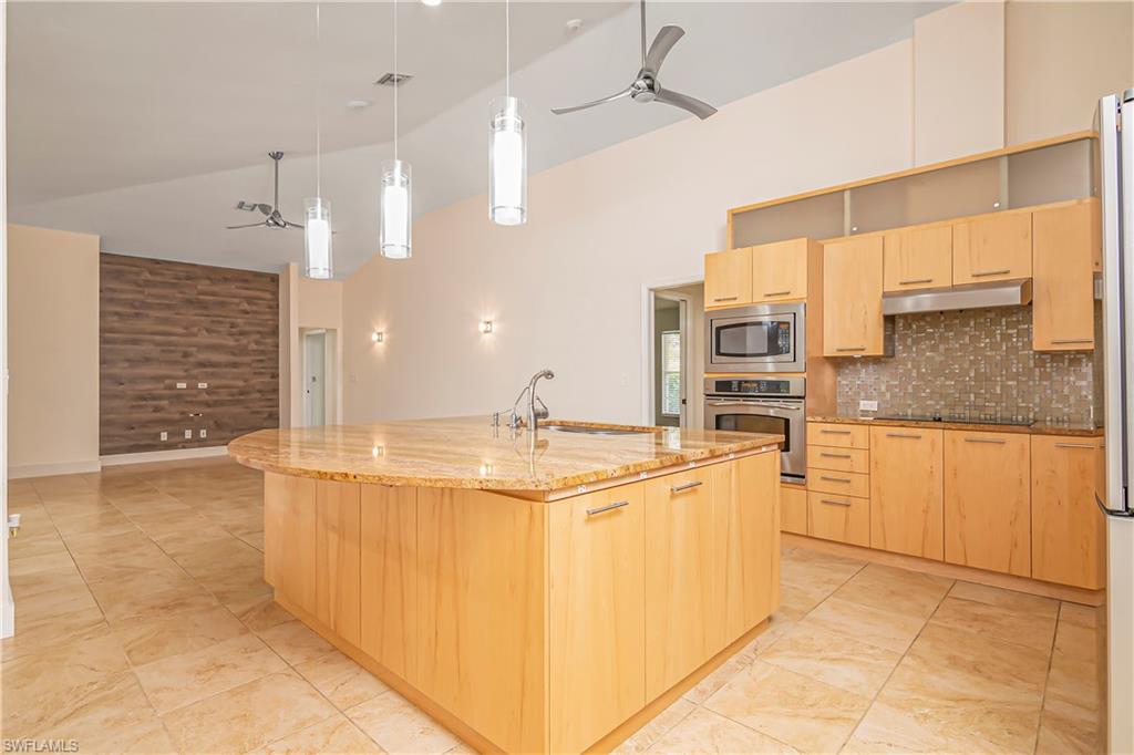 Kitchen with light brown cabinets, ceiling fan, light stone countertops, stainless steel appliances, and high vaulted ceiling