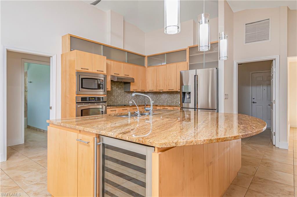 Kitchen with light brown cabinetry, light stone counters, a high ceiling, appliances with stainless steel finishes, and wine cooler