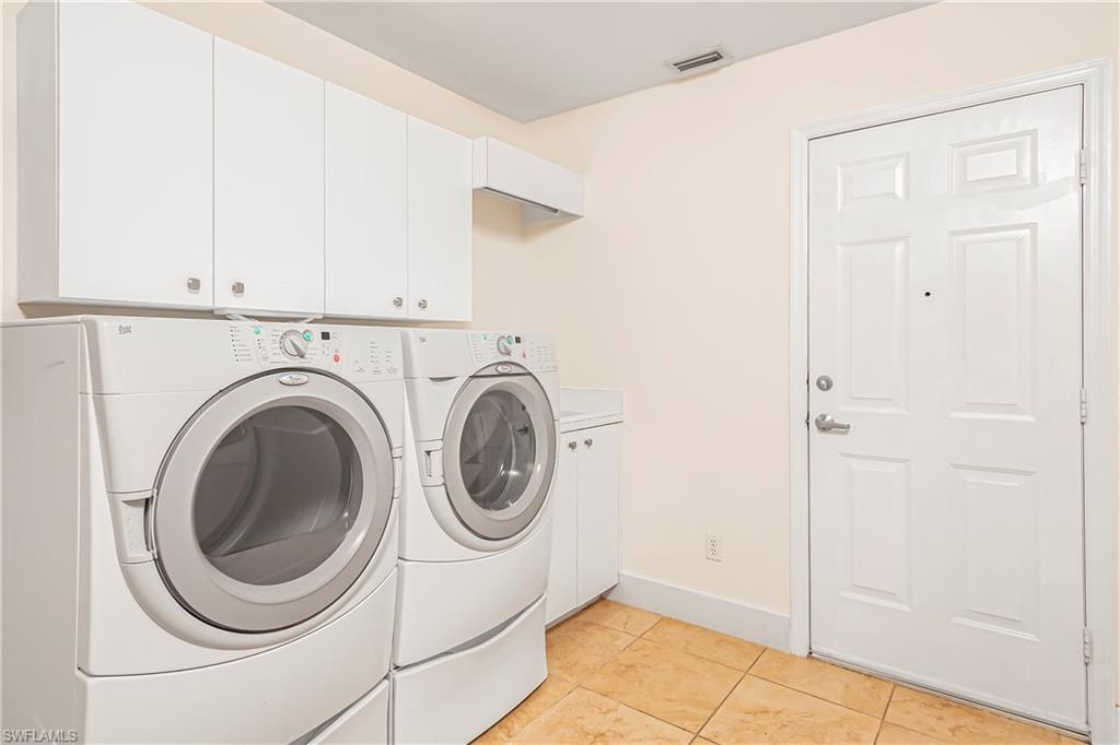 Laundry room featuring light tile patterned floors, washing machine and clothes dryer, and cabinet space