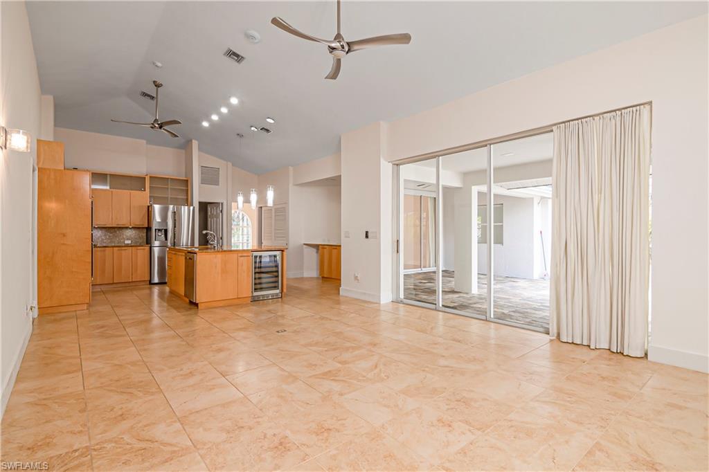 Unfurnished living room with ceiling fan, beverage cooler, and high vaulted ceiling