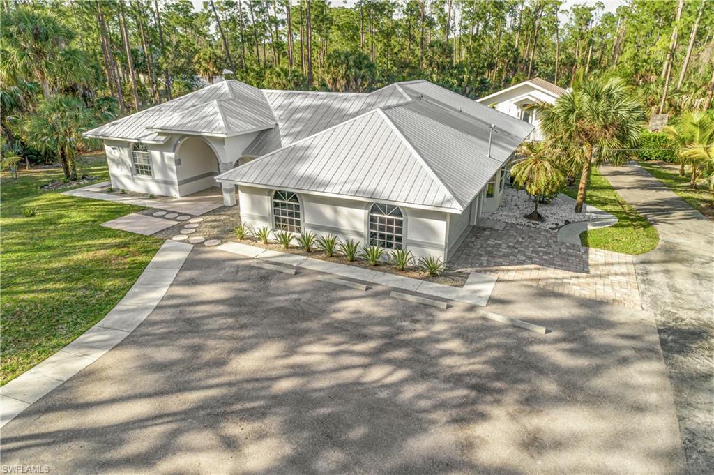 View of home's exterior with a metal roof, a lawn, driveway, and view of scattered trees
