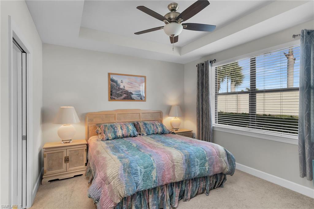 Bedroom with a raised ceiling, a ceiling fan, and light carpet