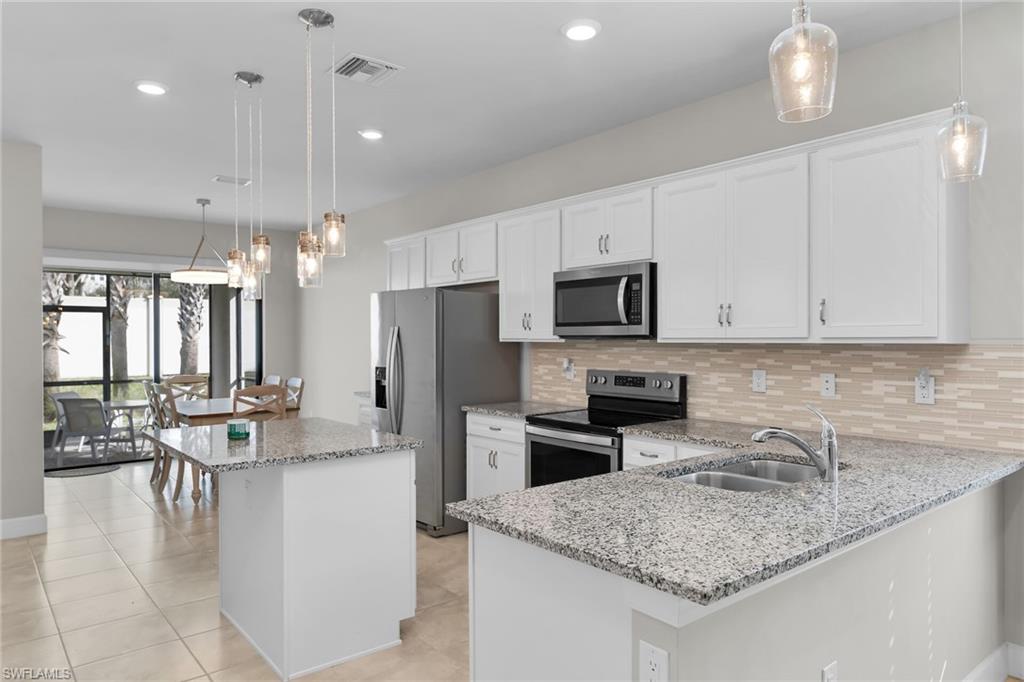 Kitchen featuring hanging light fixtures, light stone countertops, stainless steel appliances, decorative backsplash, and white cabinets