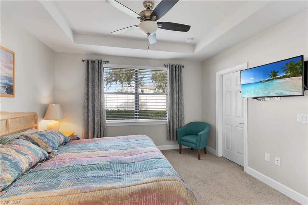 Bedroom featuring a raised ceiling, light colored carpet, and a ceiling fan