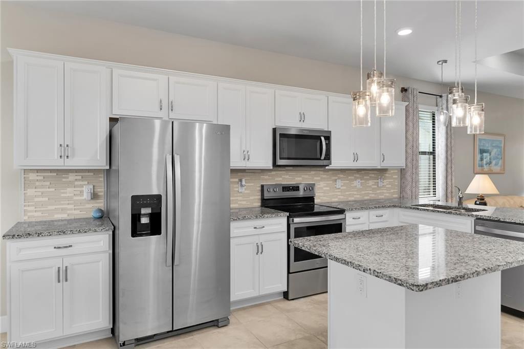 Kitchen featuring stainless steel appliances, light stone countertops, decorative light fixtures, white cabinets, and recessed lighting
