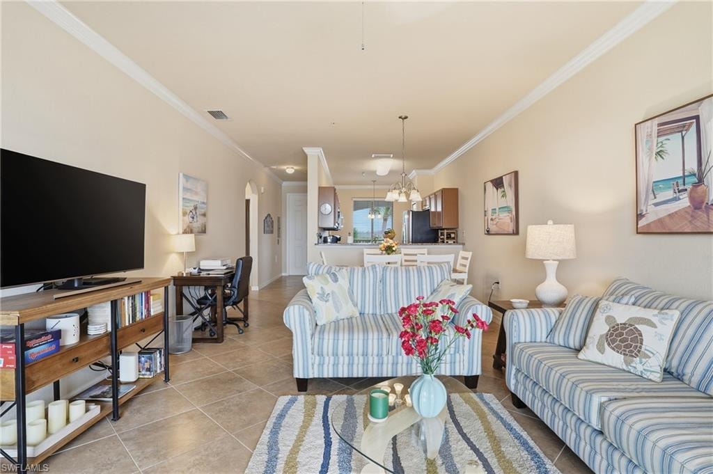 Living room featuring crown molding, light tile patterned flooring, a chandelier, and arched walkways