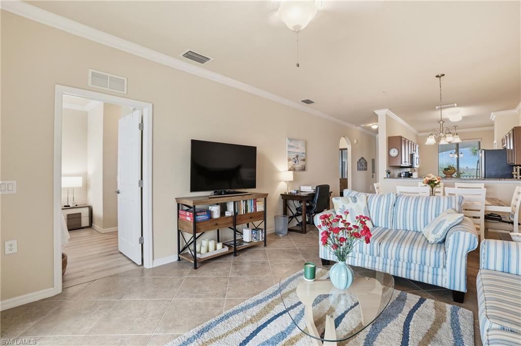 Living room with ornamental molding, arched walkways, light tile patterned floors, and a chandelier