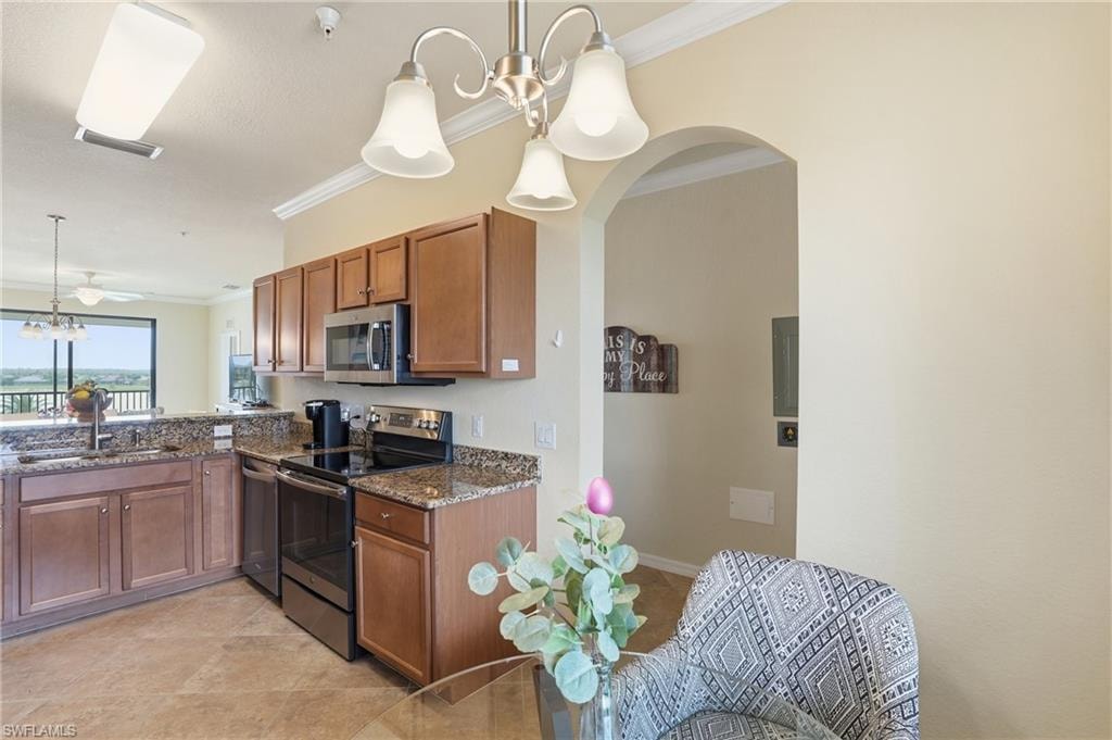 Kitchen featuring a chandelier, decorative light fixtures, brown cabinets, appliances with stainless steel finishes, and ornamental molding