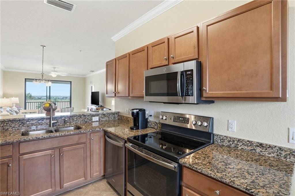 Kitchen with stainless steel appliances, ornamental molding, brown cabinets, hanging light fixtures, and dark stone countertops