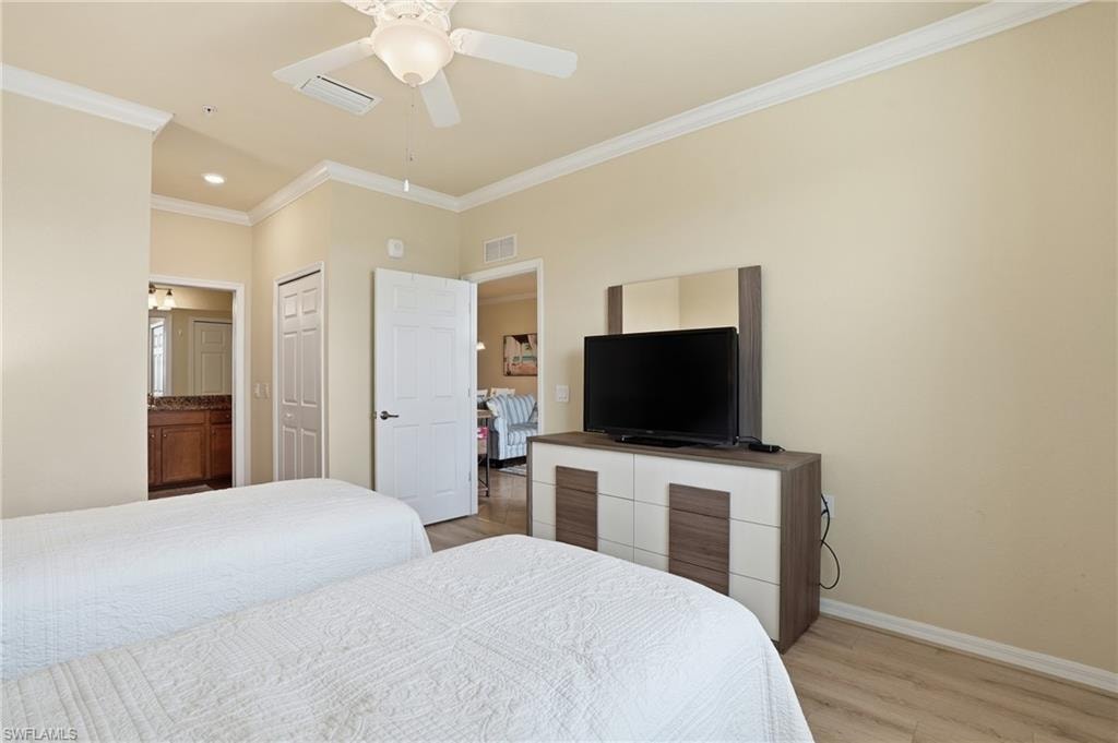 Bedroom with ornamental molding, light wood-style flooring, connected bathroom, ceiling fan, and a closet
