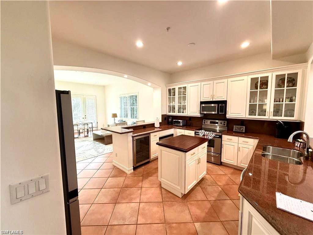 Kitchen featuring arched walkways, appliances with stainless steel finishes, light tile patterned floors, wine cooler, and recessed lighting