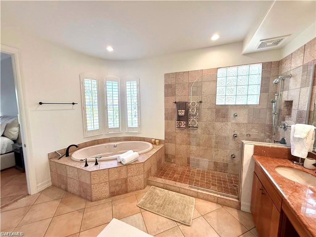 Ensuite bathroom with vanity, walk in shower, light tile patterned floors, a bath, and recessed lighting