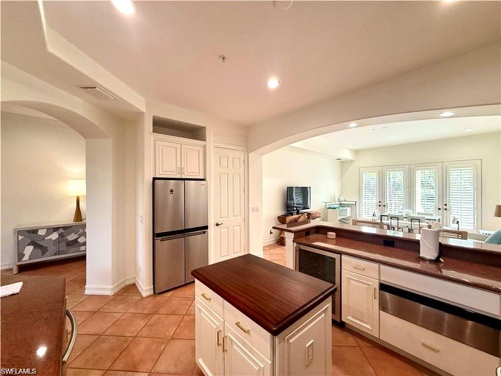 Kitchen featuring arched walkways, freestanding refrigerator, a warming drawer, recessed lighting, and white cabinetry