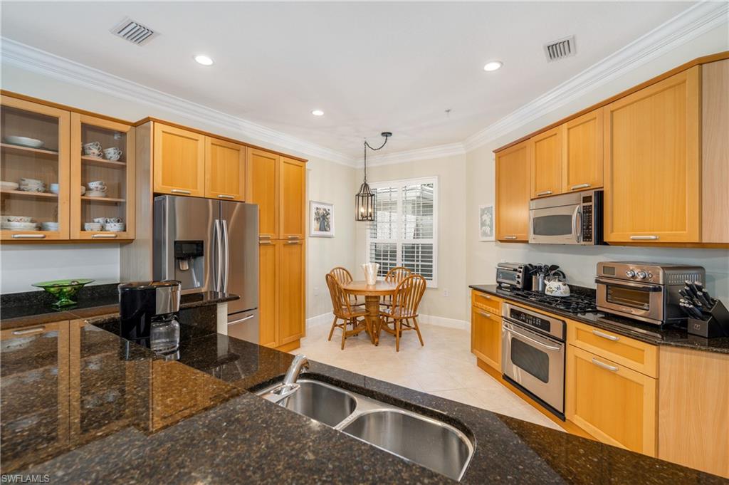 Kitchen featuring ornamental molding, stainless steel appliances, glass insert cabinets, recessed lighting, and hanging light fixtures