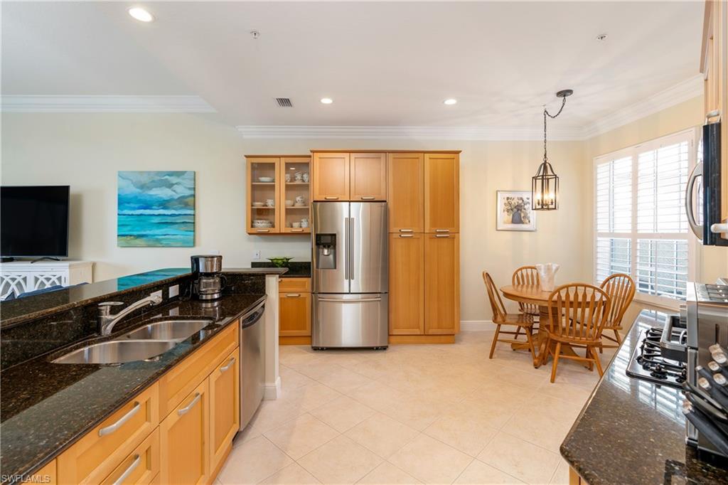 Kitchen featuring dark stone counters, glass insert cabinets, stainless steel appliances, pendant lighting, and crown molding