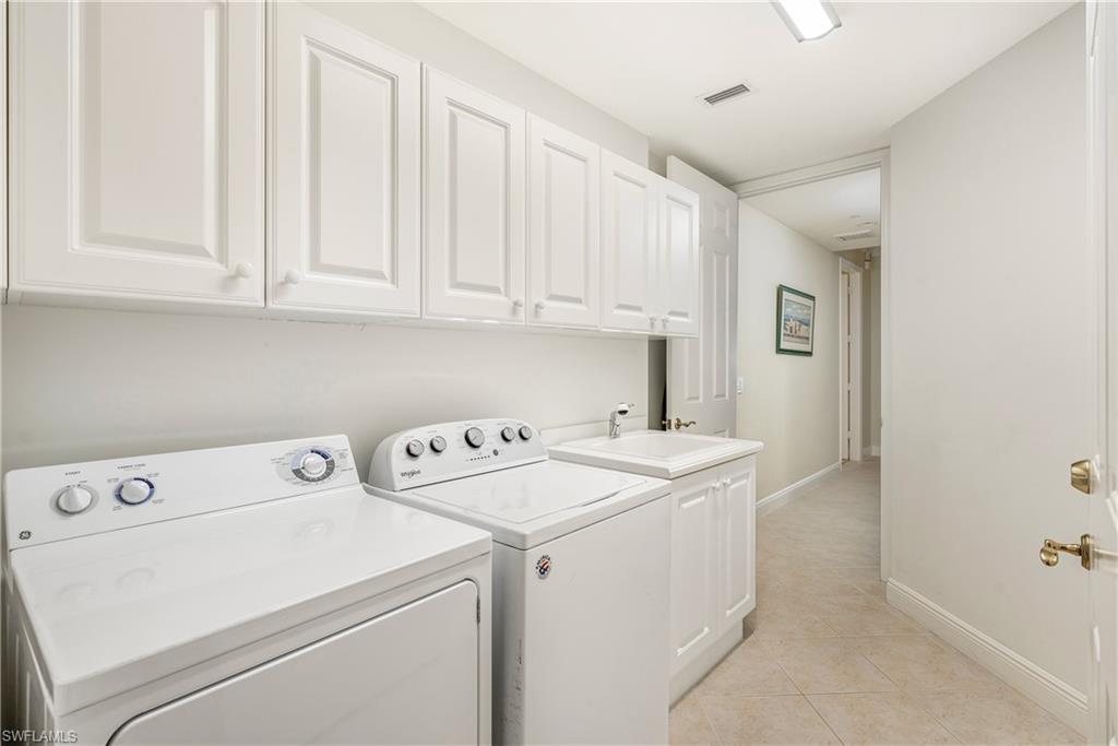 Laundry area with light tile patterned floors, washing machine and clothes dryer, and cabinet space