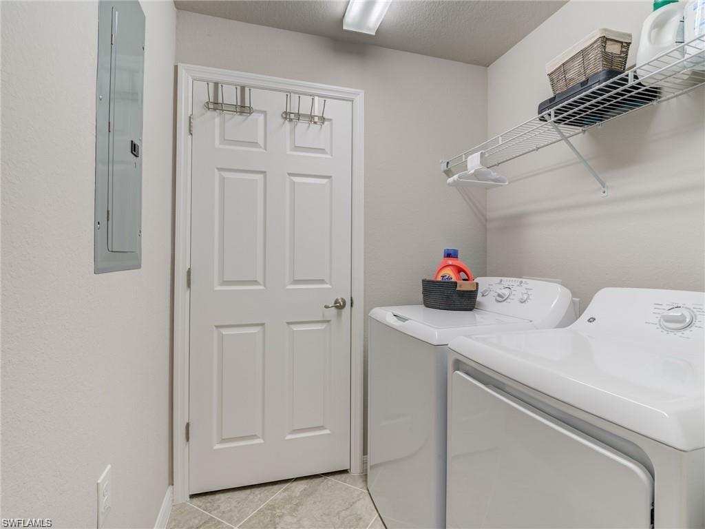 Laundry area with washer and clothes dryer, light tile patterned flooring, a textured ceiling, and electric panel