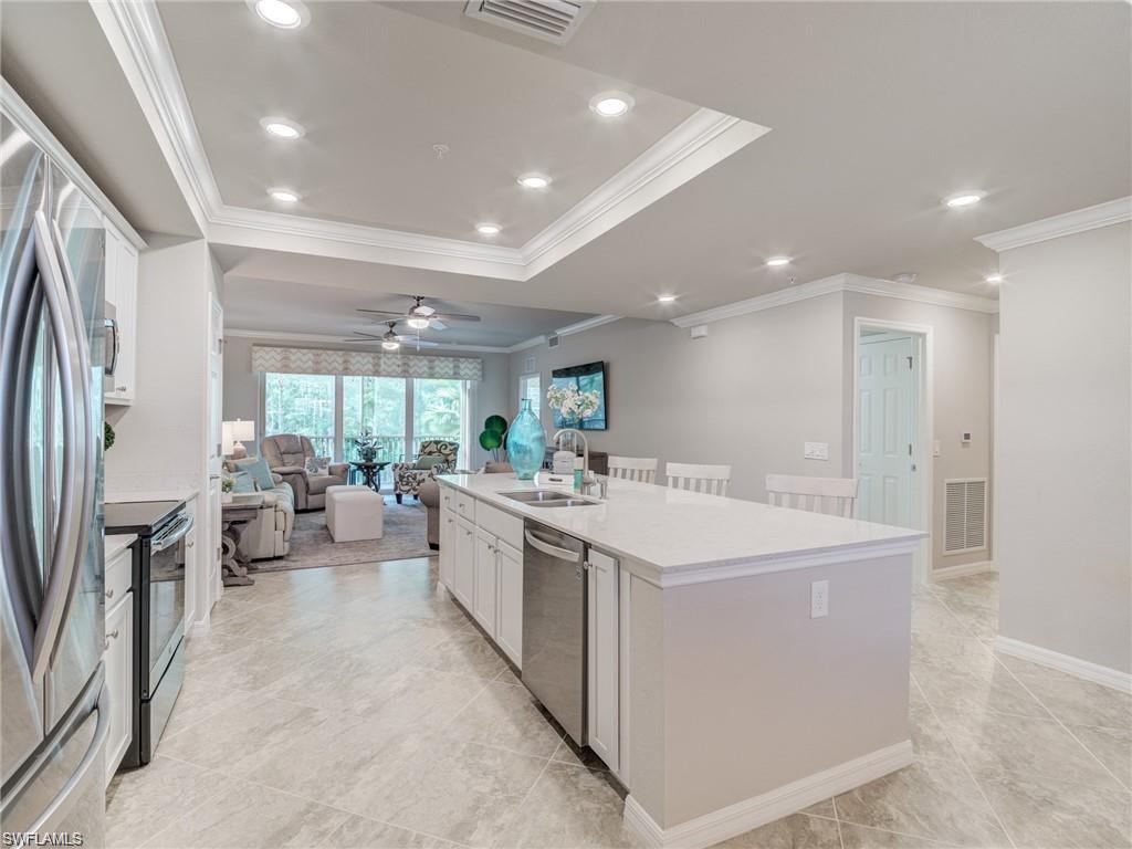 Kitchen with sink, stainless steel appliances, an island with sink, white cabinets, and ornamental molding