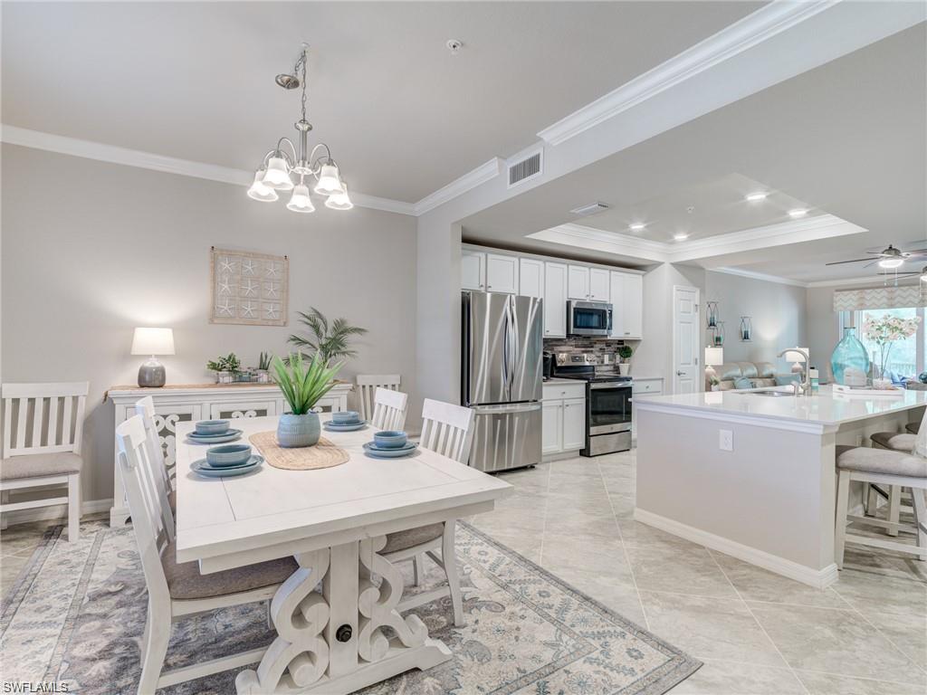 Tiled dining space with ceiling fan with notable chandelier, a raised ceiling, crown molding, and sink