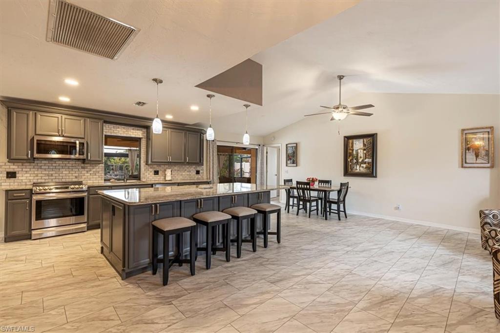 Kitchen with a breakfast bar area, stainless steel appliances, decorative light fixtures, light stone countertops, and backsplash