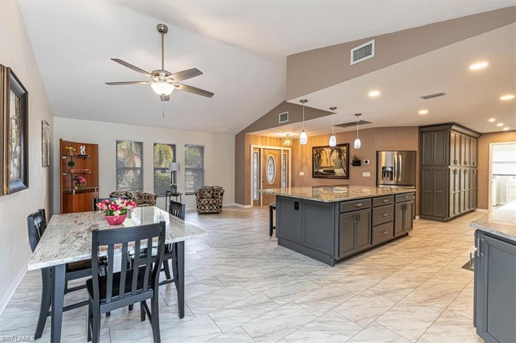 Kitchen featuring plenty of natural light, light stone counters, a kitchen bar, decorative light fixtures, and vaulted ceiling