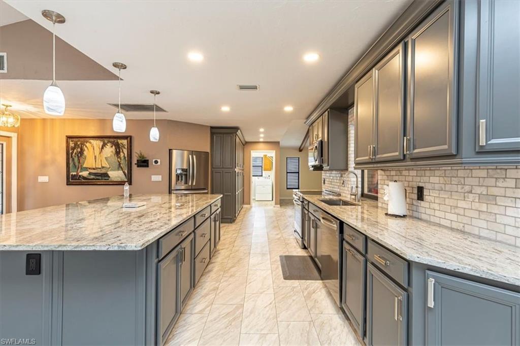 Kitchen featuring hanging light fixtures, light stone counters, appliances with stainless steel finishes, light marble finish floors, and a large island