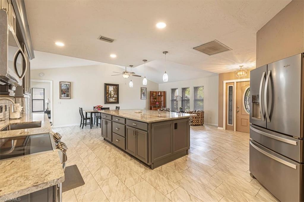 Kitchen with stainless steel appliances, light stone countertops, lofted ceiling, hanging light fixtures, and light marble finish flooring