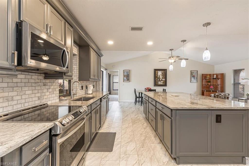 Kitchen featuring a ceiling fan, appliances with stainless steel finishes, pendant lighting, light stone countertops, and vaulted ceiling