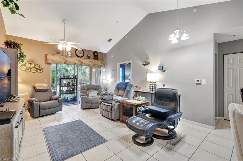 Living area with light tile patterned floors, high vaulted ceiling, ceiling fan, and a chandelier
