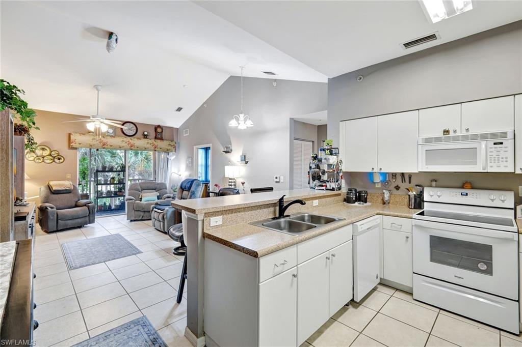 Kitchen with white appliances, white cabinets, hanging light fixtures, a peninsula, and a breakfast bar area