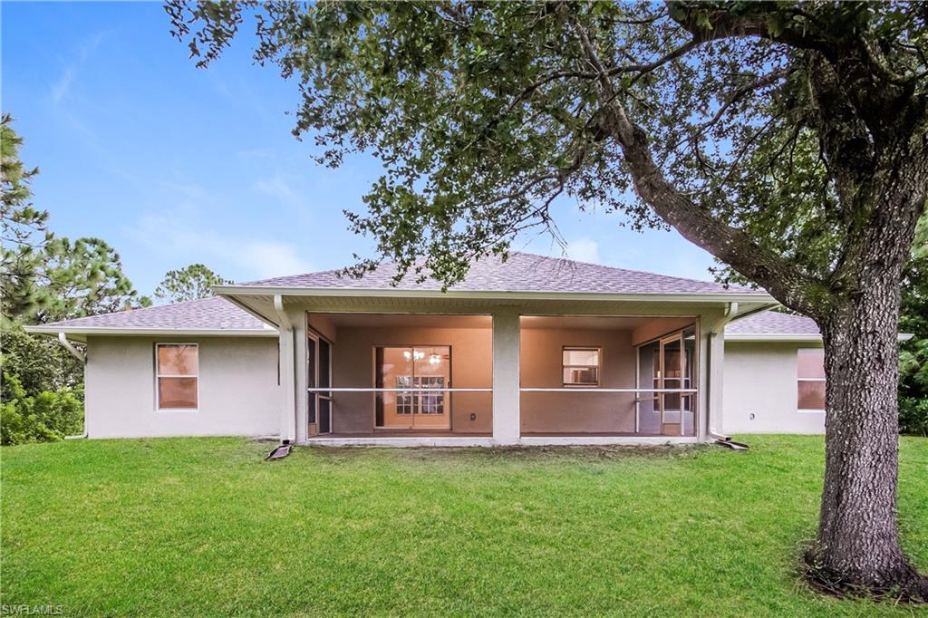 Rear view of property with stucco siding, a yard, and a shingled roof