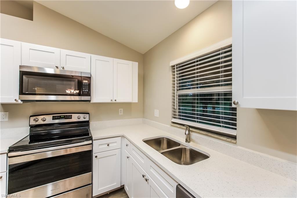 Kitchen with appliances with stainless steel finishes, white cabinetry, light stone counters, and lofted ceiling