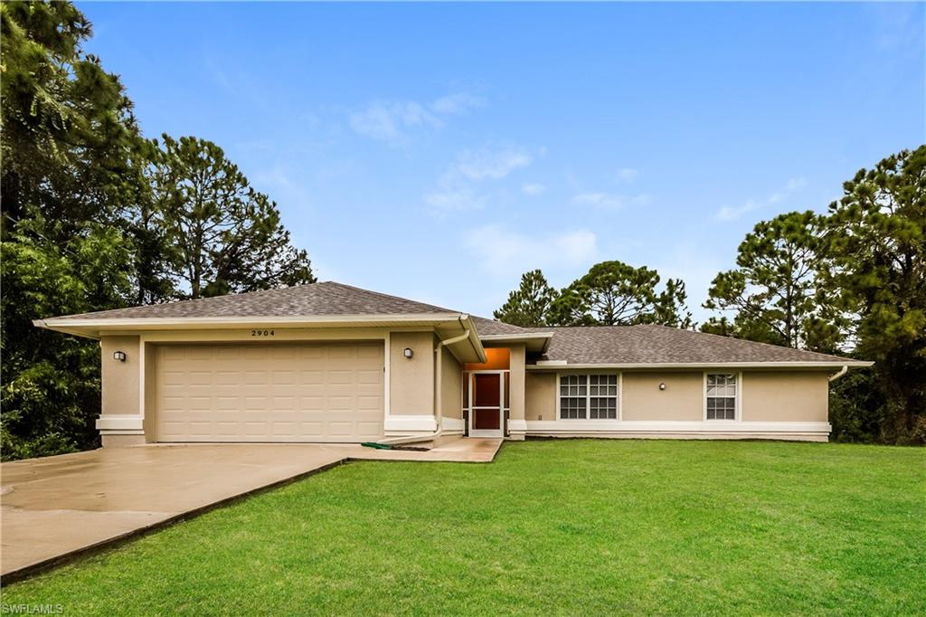 View of front of property with stucco siding, concrete driveway, a front yard, a shingled roof, and an attached garage
