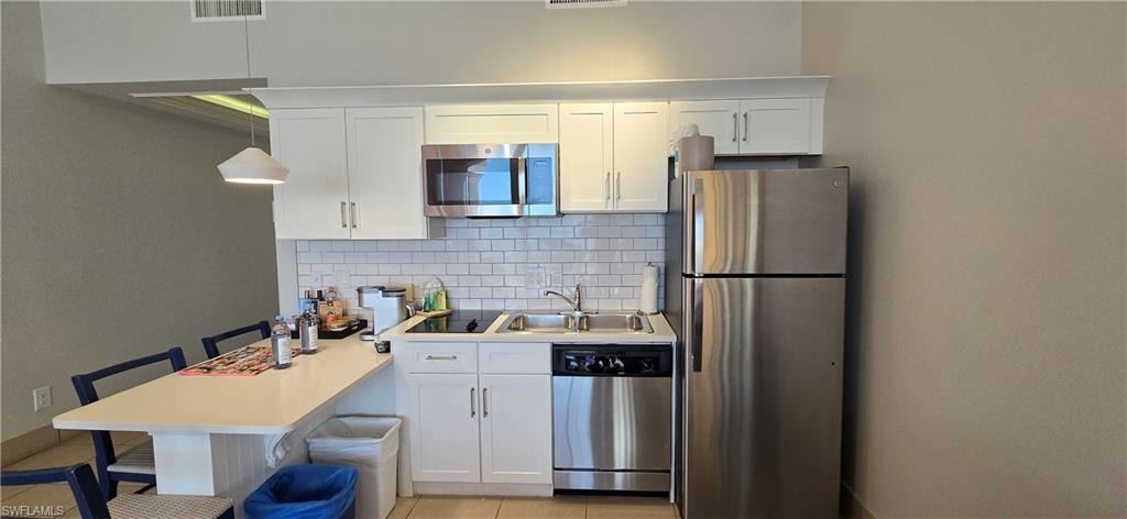 Kitchen with appliances with stainless steel finishes, white cabinets, light countertops, decorative backsplash, and hanging light fixtures
