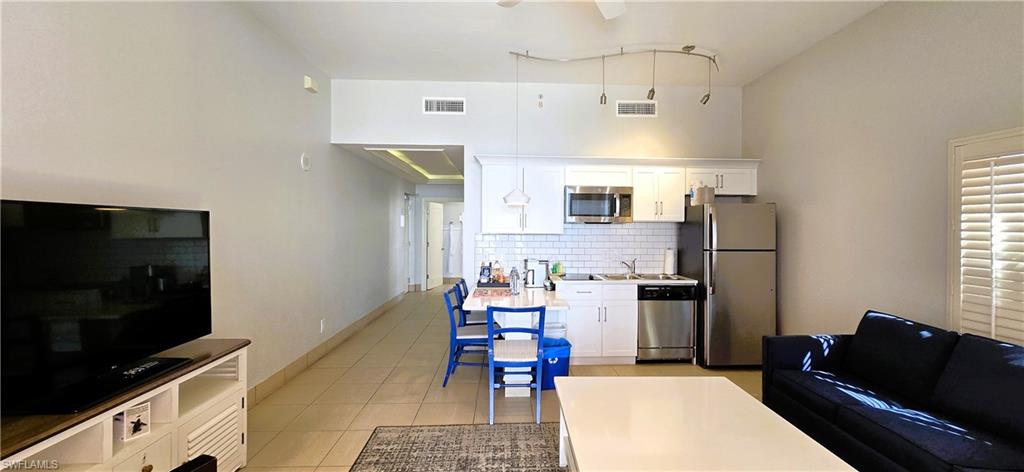 Kitchen with white cabinets, light tile patterned flooring, stainless steel appliances, hanging light fixtures, and a towering ceiling