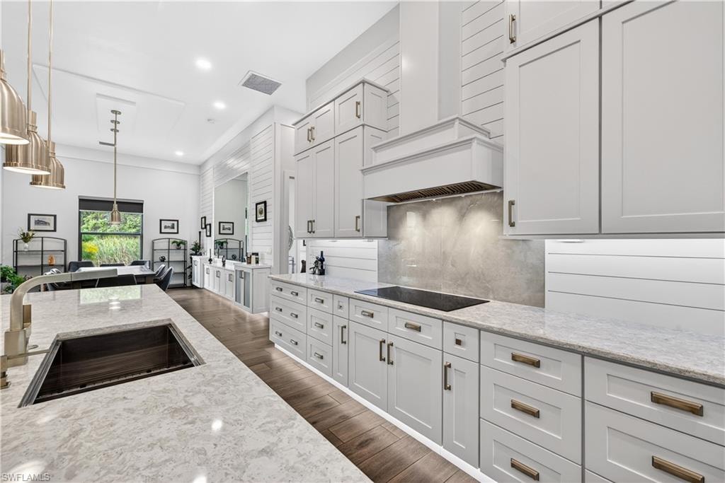 Kitchen with recessed lighting, light stone counters, premium range hood, white cabinetry, and decorative light fixtures