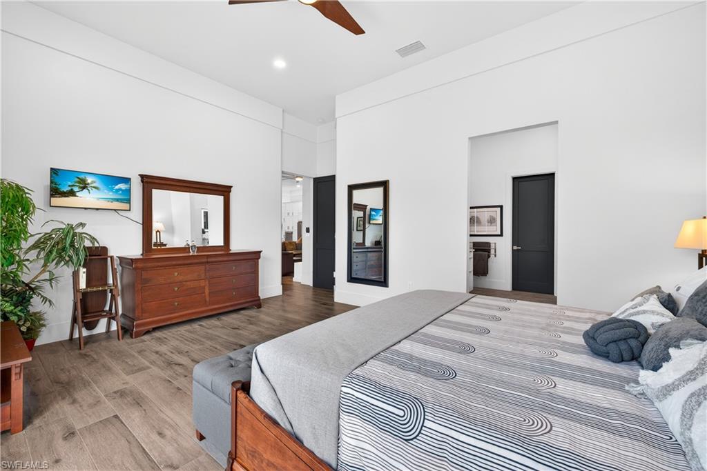 Bedroom with wood finished floors, ceiling fan, a towering ceiling, and connected bathroom