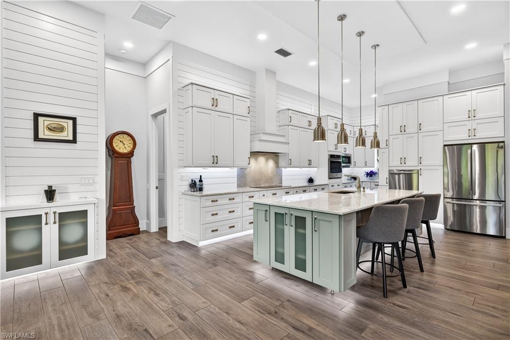 Kitchen with white cabinetry, appliances with stainless steel finishes, decorative light fixtures, a kitchen breakfast bar, and an island with sink