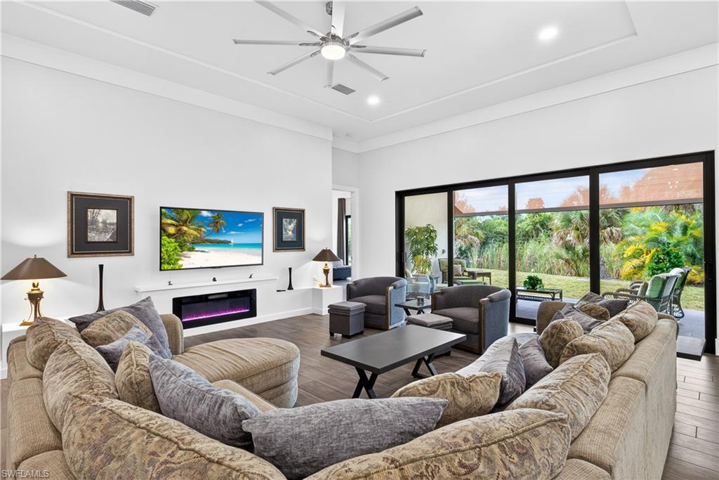 Living room with hardwood / wood-style flooring, a glass covered fireplace, ceiling fan, recessed lighting, and a high ceiling