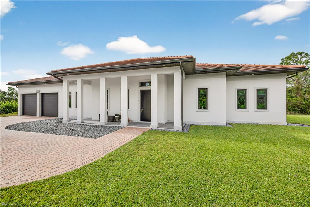 View of front facade featuring decorative driveway, stucco siding, a front yard, and a garage