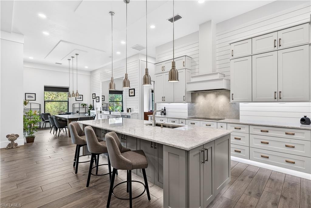 Kitchen with hanging light fixtures, light stone counters, dark wood-type flooring, custom range hood, and tasteful backsplash