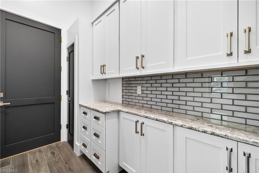 Bar area featuring light stone counters, white cabinetry, wood finish floors, and backsplash