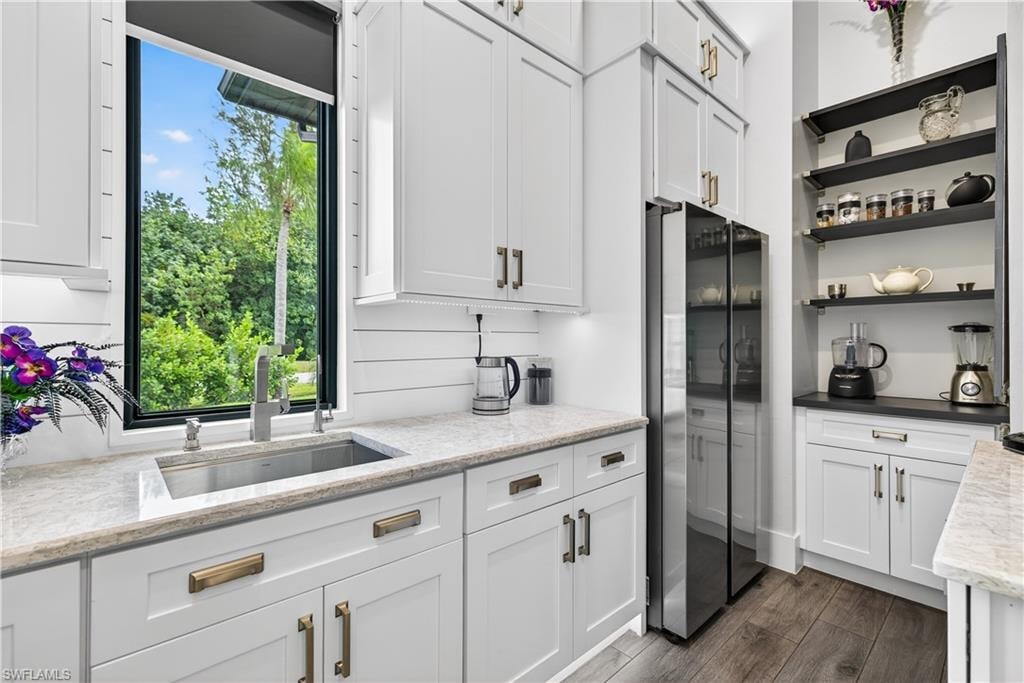 Kitchen featuring white cabinets, freestanding refrigerator, open shelves, light stone counters, and dark wood-style flooring