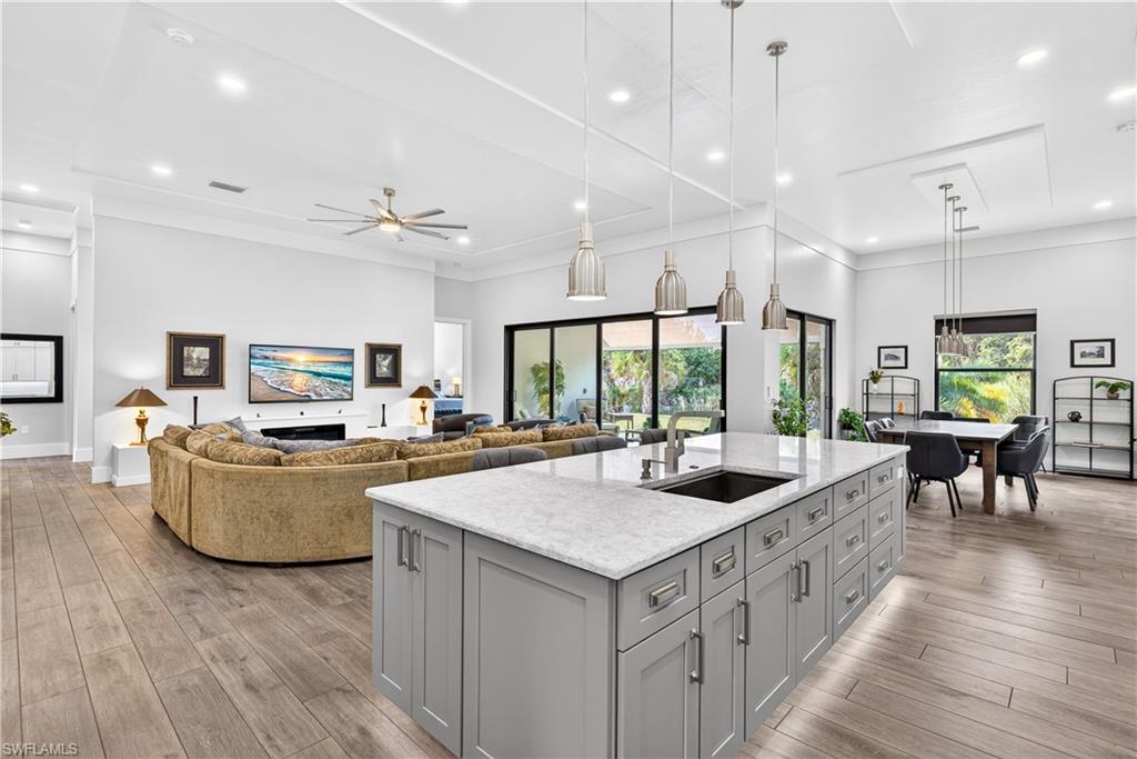 Kitchen featuring pendant lighting, an island with sink, recessed lighting, light stone countertops, and gray cabinets