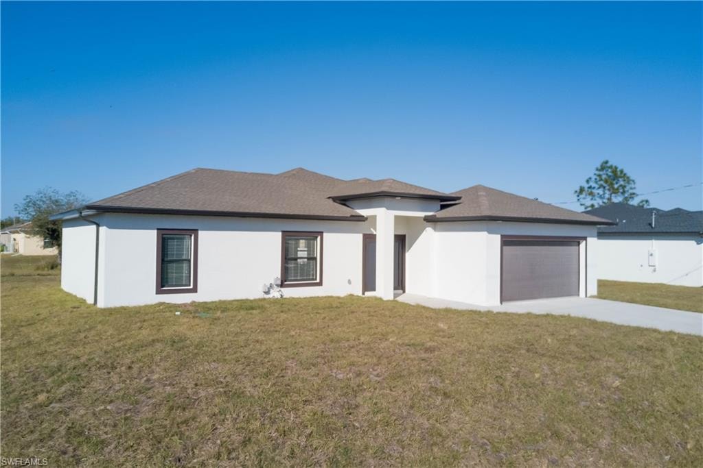 Prairie-style home with a front yard, concrete driveway, stucco siding, and an attached garage