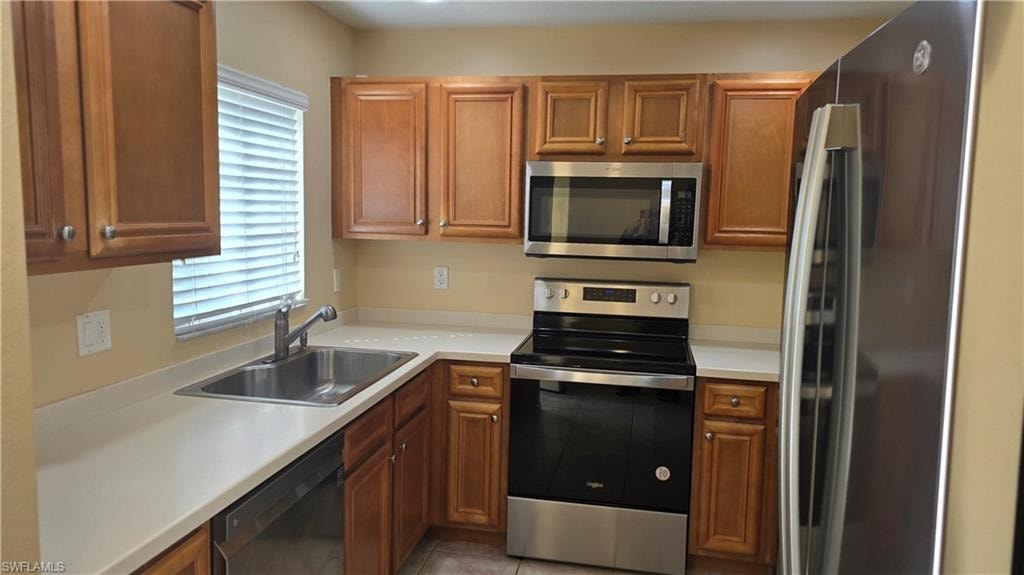 Kitchen featuring appliances with stainless steel finishes, light countertops, brown cabinetry, and light tile patterned floors