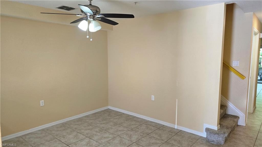 Empty room featuring light tile patterned floors, stairs, and a ceiling fan
