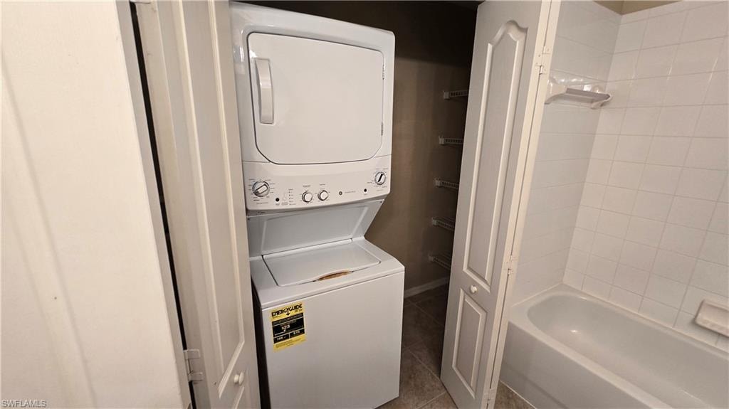 Laundry room featuring dark tile patterned flooring and estacked washer and dryer